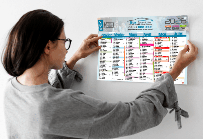 Femme accrochant un calendrier mural publicitaire 2026 dans un bureau