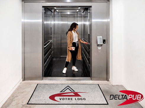 Tapis d'entrée personnalisé r-PET avec logo devant un ascenseur de bureau.